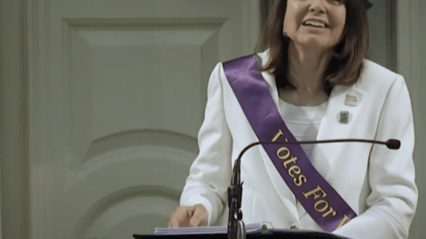 Woman stands at podium speaking.
