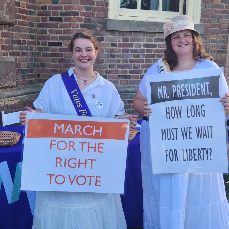 Contemporary women Marching in a suffrage parade holding signs and dressed in 1910s clothing.