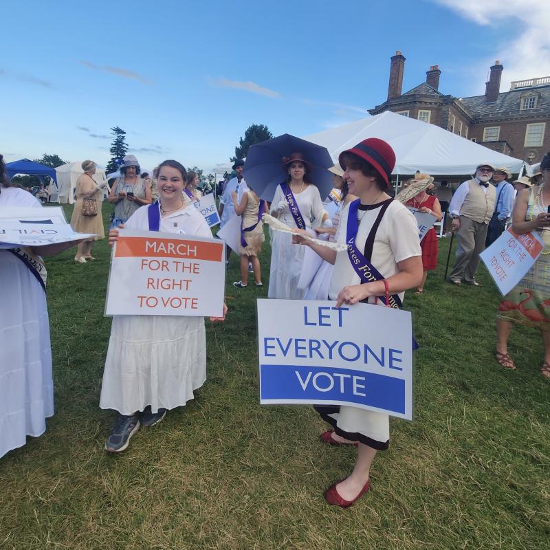 Contemporary women Marching in a suffrage parade holding signs and dressed in 1910s clothing.