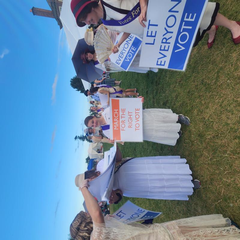 Contemporary women Marching in a suffrage parade holding signs and dressed in 1910s clothing.