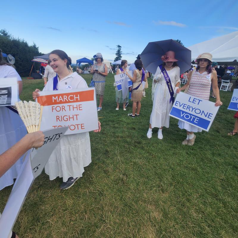 Contemporary women Marching in a suffrage parade holding signs and dressed in 1910s clothing.