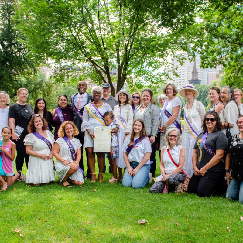 Large group of people stand outside wearing purple sashes.