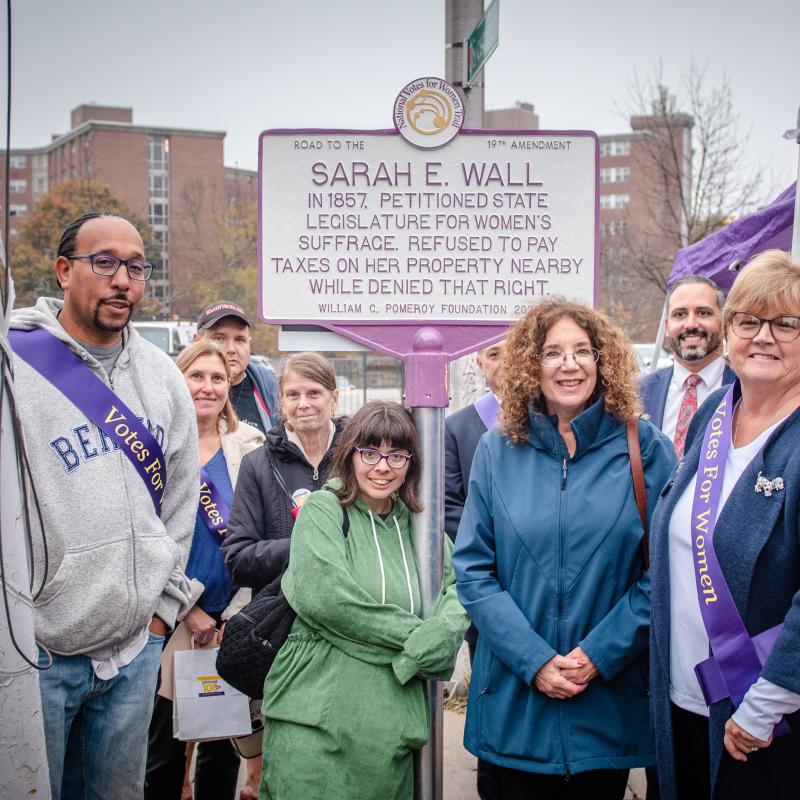 Six adults stand in front of sign.