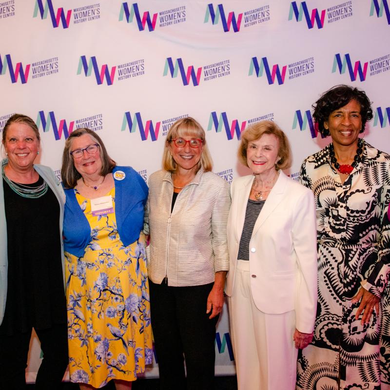Seven women stand in front of Massachusetts Women's History Center's step and repeat.