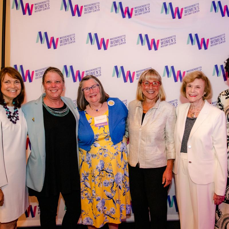 Seven women stand in front of Massachusetts Women's History Center's step and repeat.