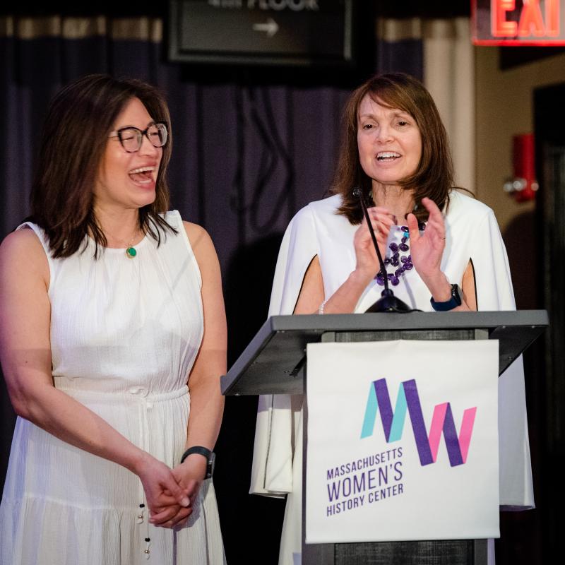 Two women stand at podium speaking.