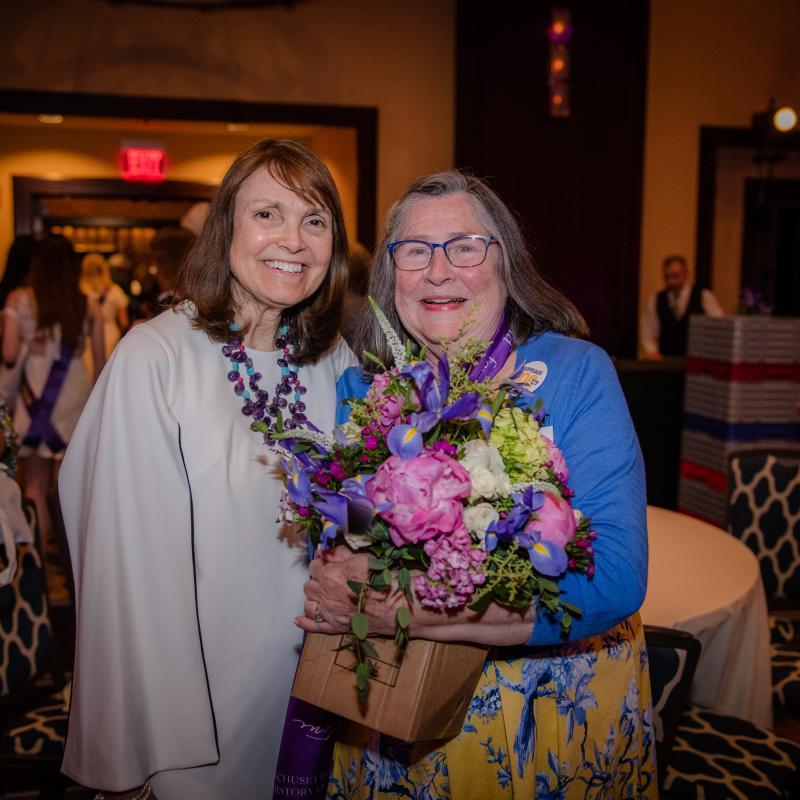 Two women stand inside smiling.