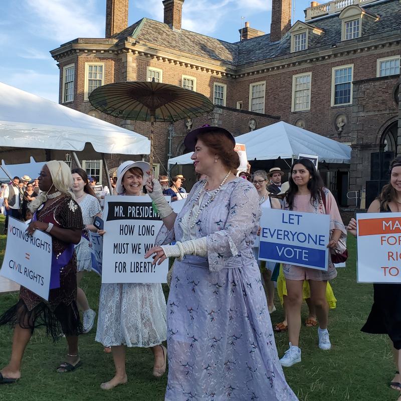 People marching on lawn holding signs.