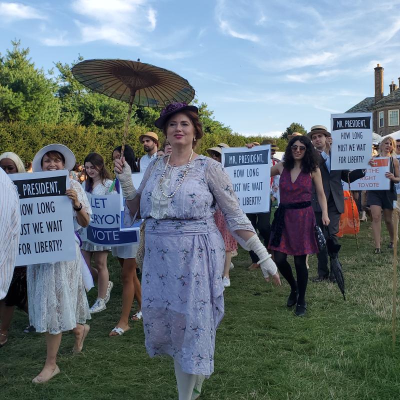 People marching on lawn holding signs.