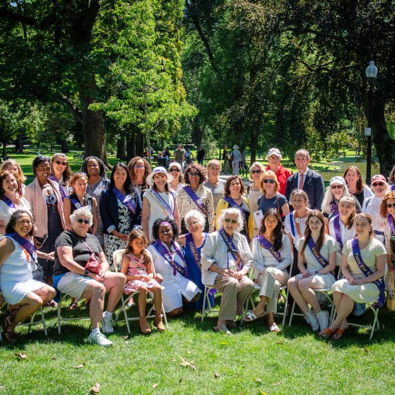 Group of adults and 1 child stand and sit outside smiling.