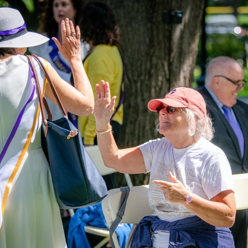 Woman sits outside wearing purple sash.