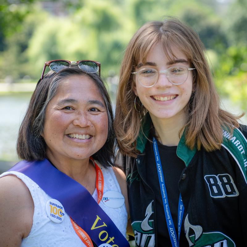 Two women wearing purple sashes stand outside smiling.