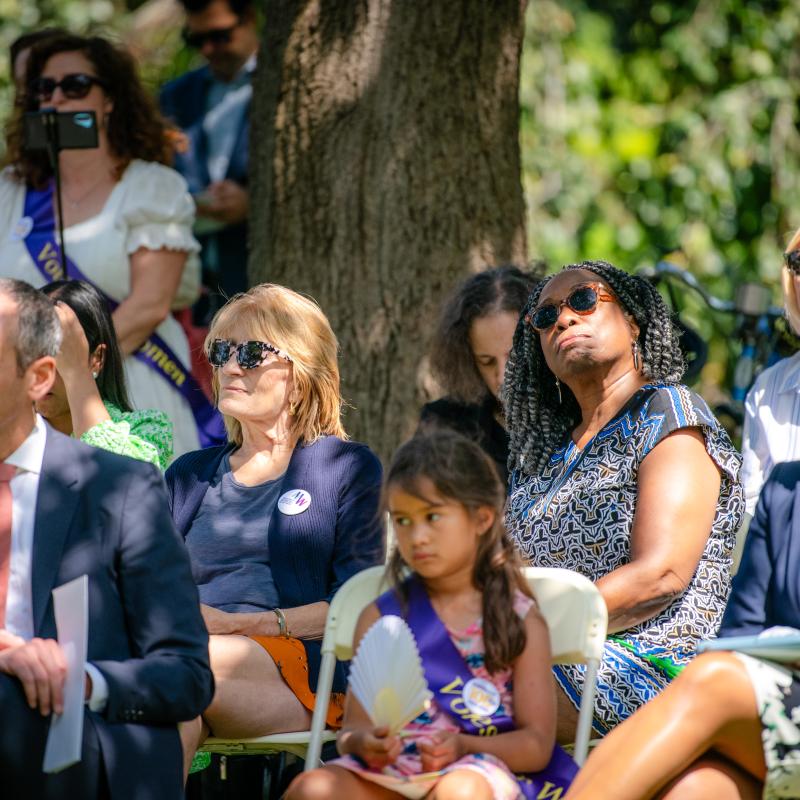 Group of women sit outside wearing purple sashes.