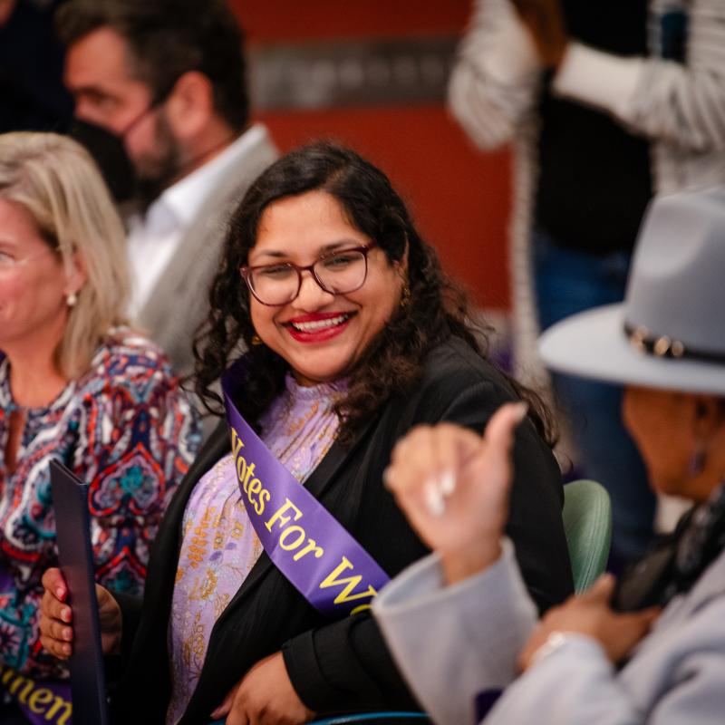 Woman wearing purple sash sitting and smiling.