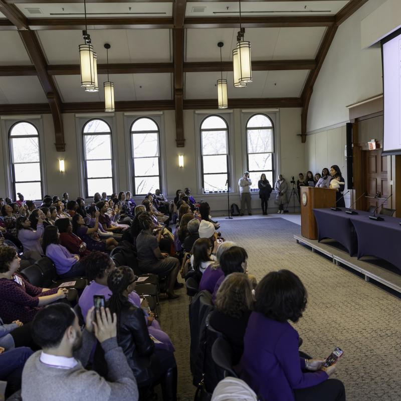 A crowd of people seated and listening to a speaker at a podium