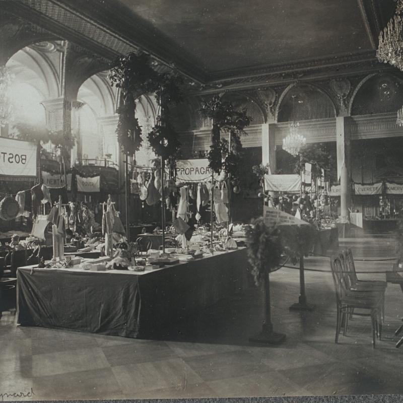 Black and white photograph of ornate room with multiple booths for suffrage bazaar