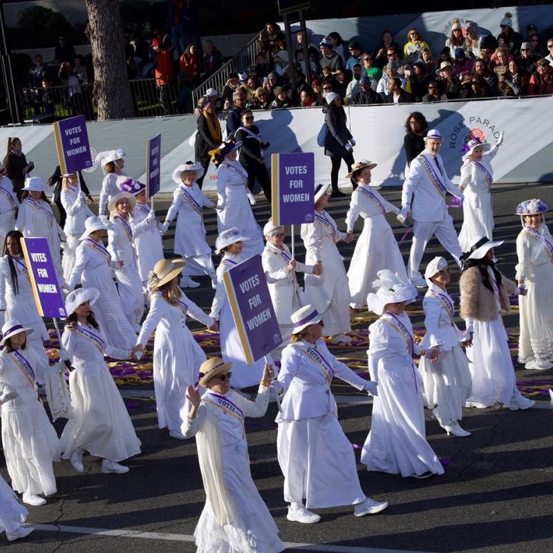 Women in white march in parade.
