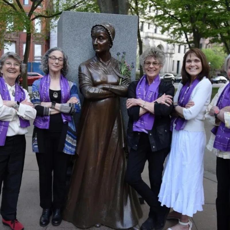 Four women stand smiling in front of monument.