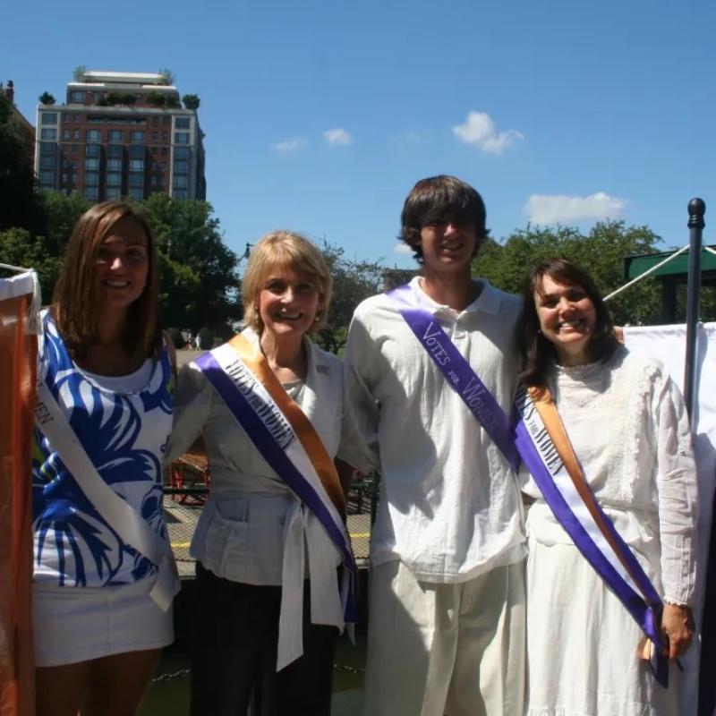 Four people stand outside in sunlight smiling.