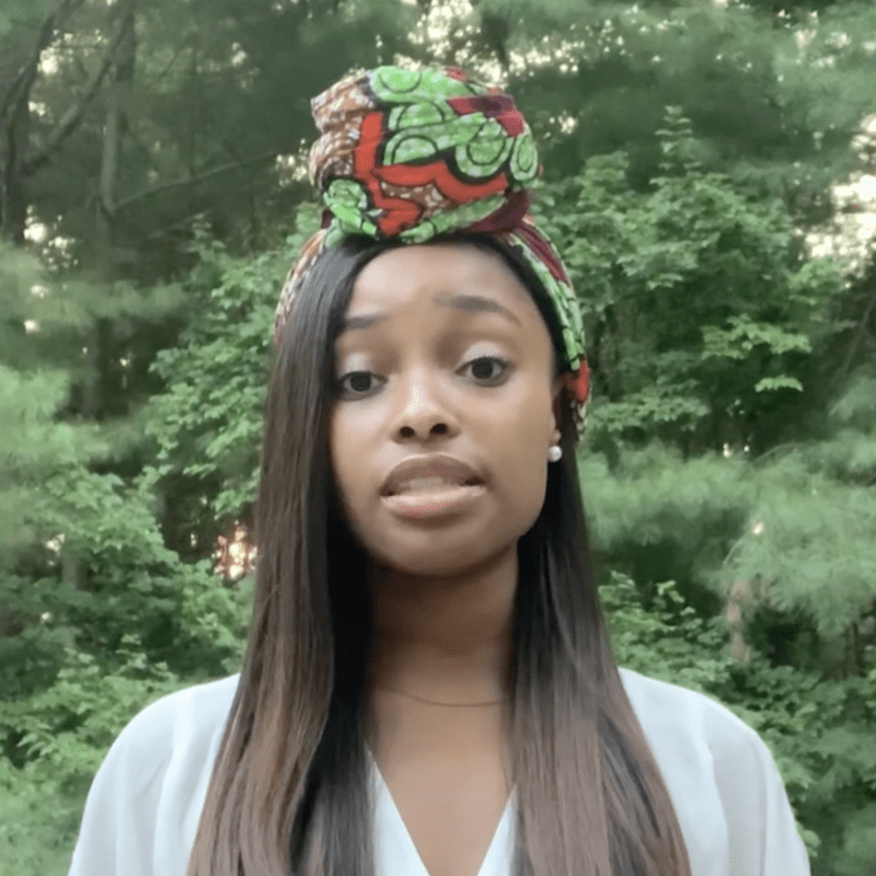 Woman stands outdoors speaking.