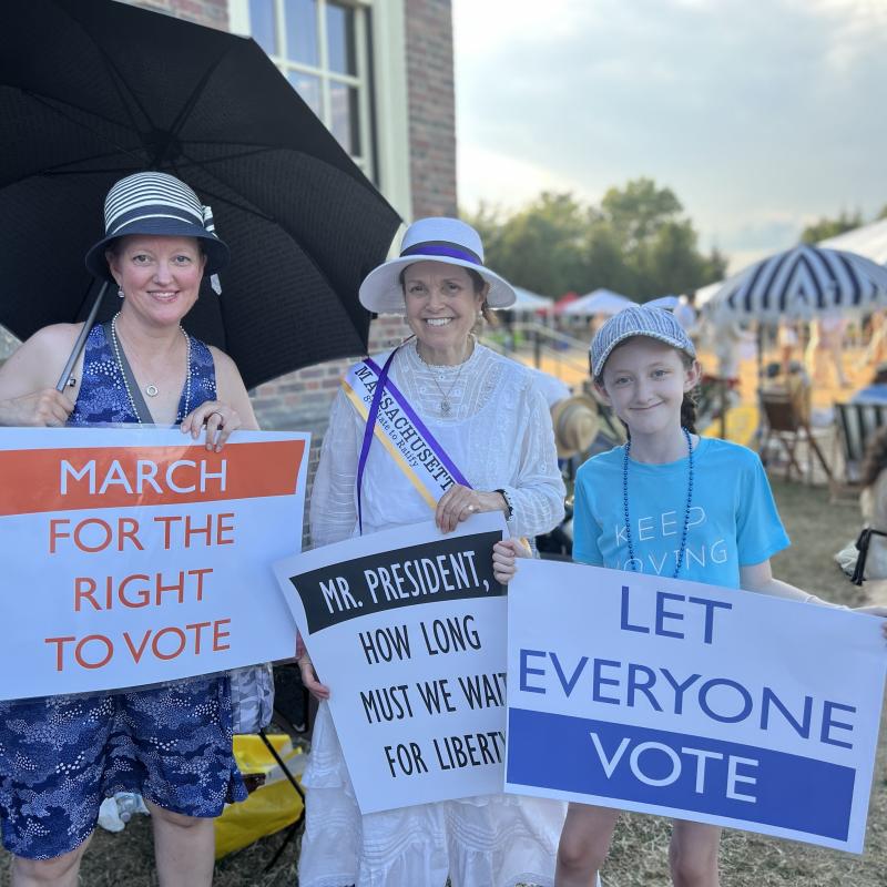 Three people stand outside holding signs.
