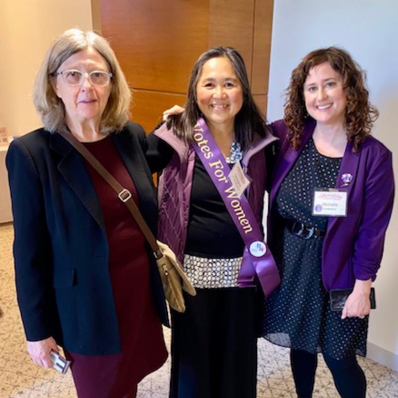 Three women stand together smiling.