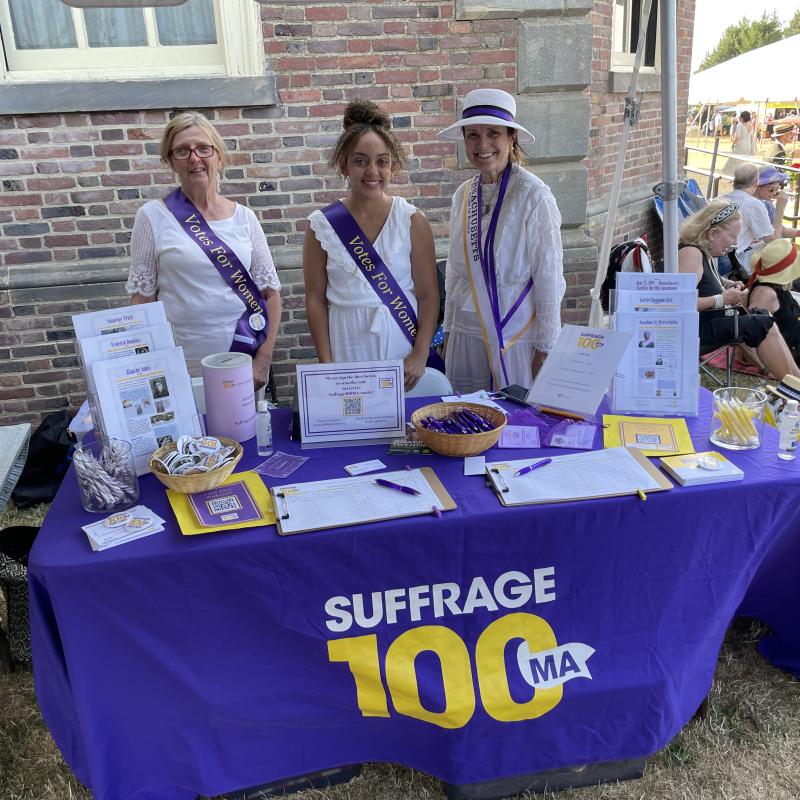 Three women stand at purple table.