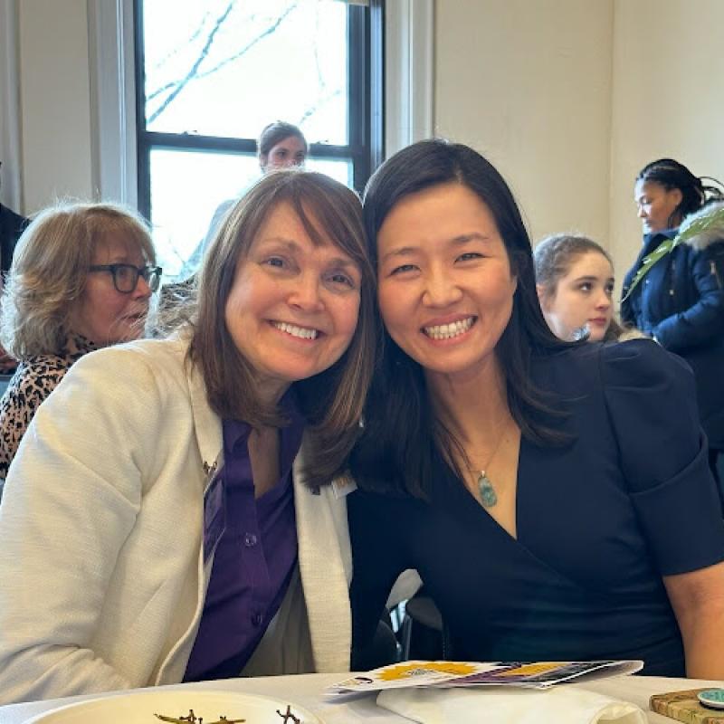 Two women sit at table smiling.