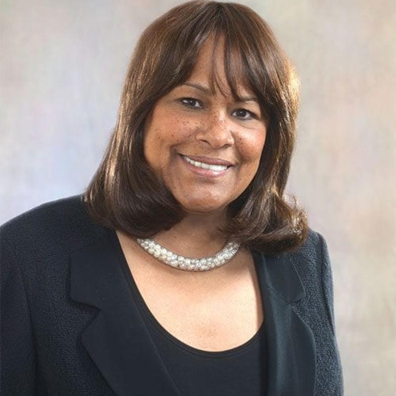 headshot of a woman smiling and wearing a black jacket and white necklace