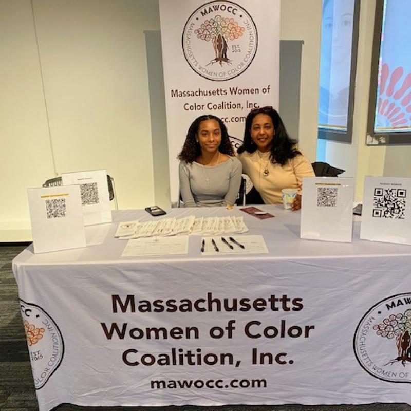 Two women sit at white table smiling.