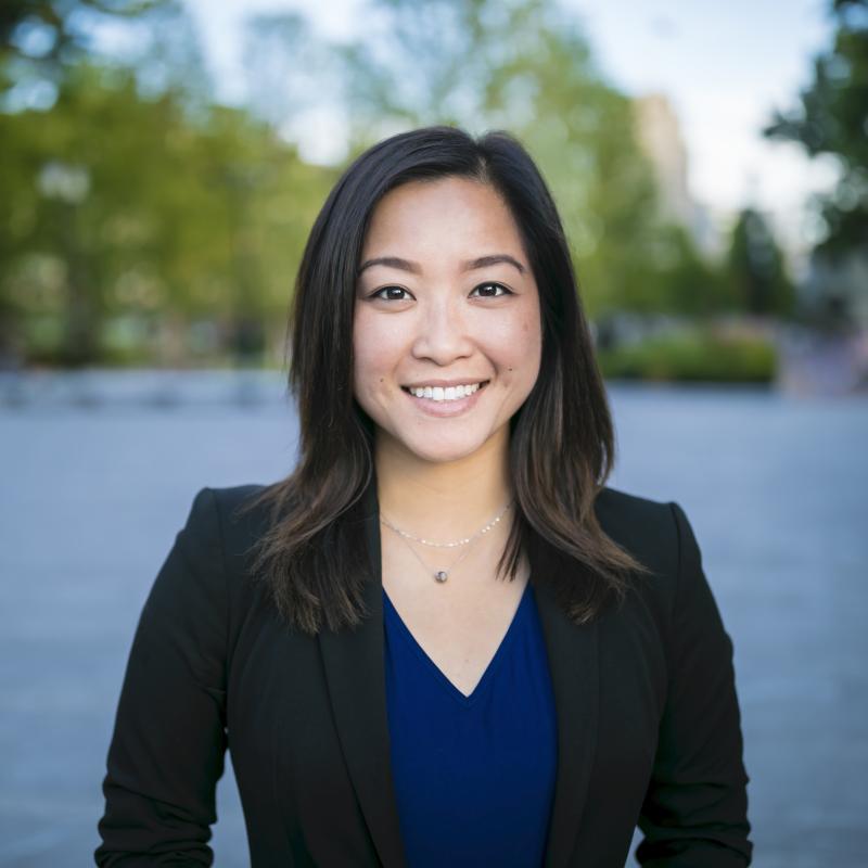 A woman wearing a black blazer standing outside and smiling.