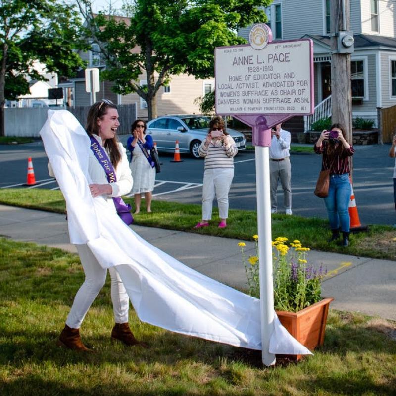 Two women wearing purple sashes stand outside smiling.