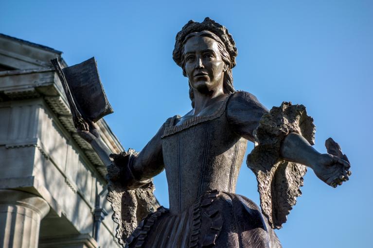 Bronze statue of Mercy Otis Warren holding a quill and book.