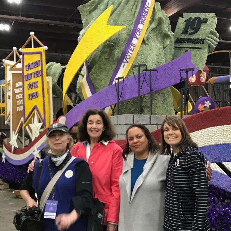 Four women stand in front of parade float.